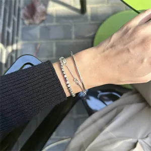 Detail shot of a minimal silver geometric bangle and beaded bracelet on a wrist