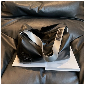 Detailansicht der großen Kunstledertasche mit Kontrastgurt auf einem schwarzen Sofa