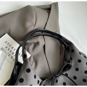 Detailed texture of grey polka dot bucket bag with black handles on a grey suit background