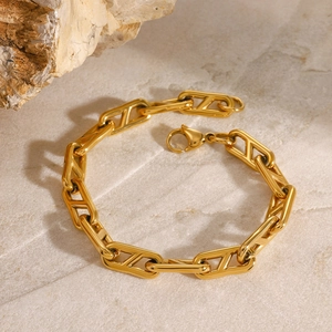 Detail view of gold stainless steel geometric chain bracelet on marble surface