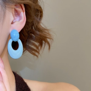Close-up of light blue acrylic oval earrings worn by a model in soft lighting