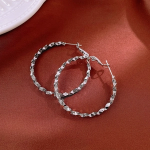 Close-up of silver geometric hoop earrings with rhombic facets on silk background