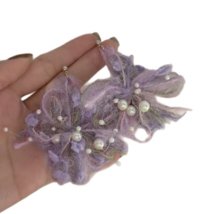 Handmade purple yarn flower earrings with pearls shown held in hand for size context
