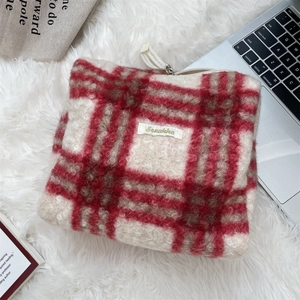 Detailweergave van de rood-witte geruite pluche make-uptas op een zacht wit tapijt