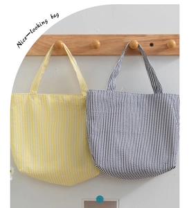Close-up of yellow and grey striped tote bags in seersucker fabric hanging on wooden hooks