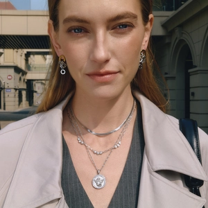 Détail de colliers argentés superposés avec pendentif ange et chaîne strass sur modèle