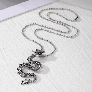 Detailed close-up of a silver dragon pendant with bead chain on a white textured surface