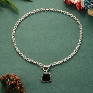 Detail of silver OT buckle chain necklace featuring a black trapezoid pendant on green texture
