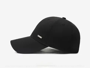 Detail of minimalist black baseball cap featuring a polished silver metal logo plate