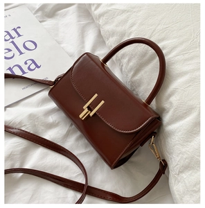 Close-up of retro reddish-brown leather handbag with golden H-shaped clasp on white fabric