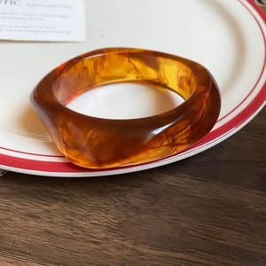Detailed view of amber resin wide bangle with marbled textures on a white ceramic plate