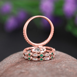 Detail of rose gold rings with green emerald stones and diamonds on textured stone