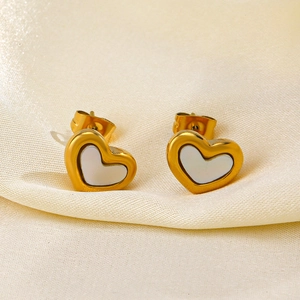 Fashionable golden heart-shaped shell earrings on silk fabric background minimalist style