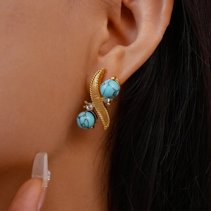 Close-up of golden leaf earrings with turquoise beads and diamonds worn by a model