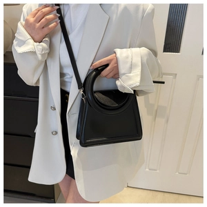 Minimalist black matte leather handbag with circular handle shown on model in white suit