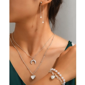 Detail of silver pearl jewelry set with moon and heart charms on a model neck