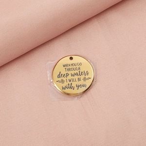 Close-up of gold stainless steel circular tag with engraved deep waters quote detail