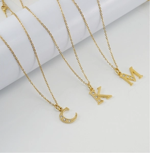 Détail de colliers en acier plaqué or 18K avec pendentifs lettres sertis de cristaux