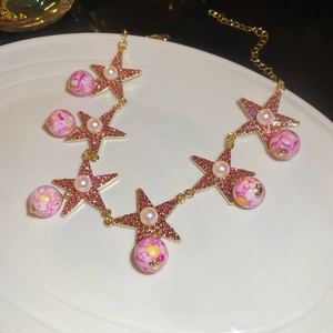 Detail of star necklace with pink stones and marble bead on white display plate