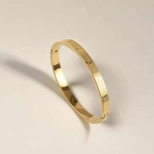Macro detail of golden stainless steel bangle with textured surface and oval clasp closure