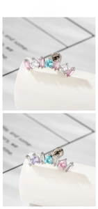 Close-up of curved ear studs with heart-shaped colorful cubic zirconia and screw-back balls