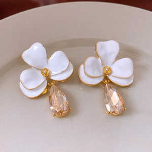 Détail de boucles d'oreilles fleurs blanches à bords dorés et cristaux en goutte