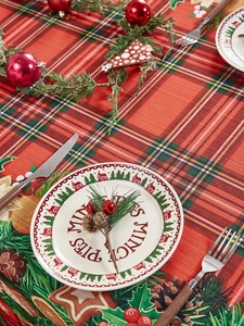 Close-up of red and green plaid Christmas tablecloth with festive plate and pine cones