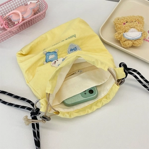 Detail der gelben Canvas-Beuteltasche mit Smartphone-Fach und gesticktem Bären-Design