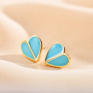 Detail shot of heart-shaped gold stud earrings with bright blue enamel on beige velvet
