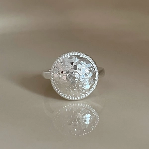 Minimalist silver hammered round signet ring with beaded edge on reflective warm surface