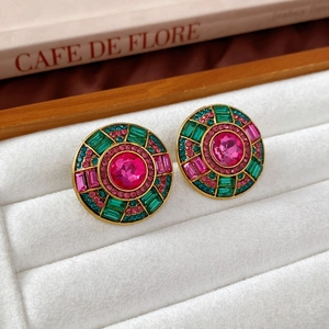 Close-up of vintage round earrings with pink crystal and green gems on white velvet