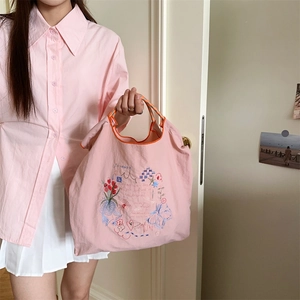 Gros plan détaillé du sac en toile rose avec broderie florale et anses rayées
