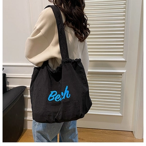 Detail of black drawstring tote bag with blue Bech lettering shown on female model