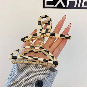 Detail of checkerboard pattern hair claws with gold metal frames in hand