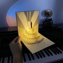 Detail of 3D pop-up birthday card with glowing multi-layer cake and warm lighting