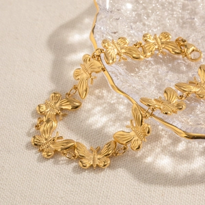 Détail du bracelet à maillons papillon dorés avec fermoir mousqueton sur un tissu texturé