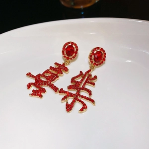 Detailed view of Xi character earrings with red rhinestones in a gold metal frame