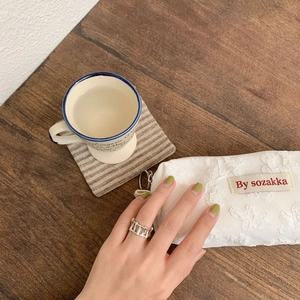 Detail of a silver geometric hollow ring shown on a finger against a cozy lifestyle background