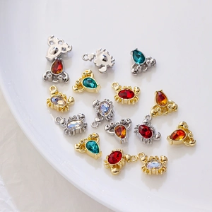 Golden and silver crab charms with colorful zirconia stones on a white ceramic plate