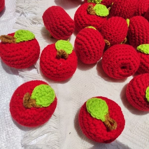 Detailed view of hand-knitted red apple keychains with green leaves on white fabric