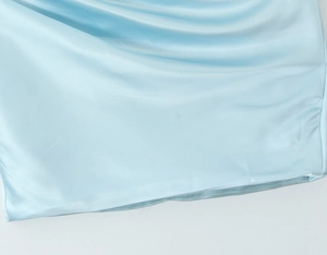 Close-up of the smooth light blue satin fabric and precise sewing details of the dress
