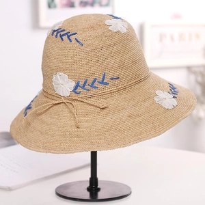 Close-up of beige raffia sun hat featuring white floral embroidery and hemp bow detail