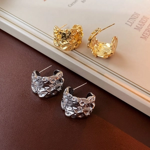 Nahaufnahme goldener und silberner C-Ohrringe mit unregelmäßiger Hammerschlag-Textur
