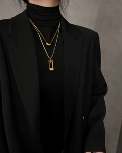 Detail of a double-layered gold necklace with cylindrical and rectangular pendants