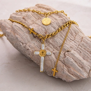 Detail of gold layered necklace with cross and Saint Benedict medal on stone surface