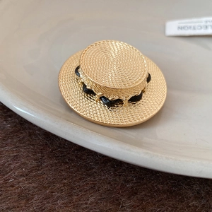 Detaillierte Nahaufnahme der goldenen Strohhut-Brosche mit Textur und schwarzem Band