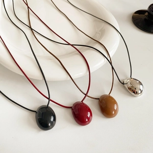 Vue détaillée de pendentifs en résine en forme de galet avec cordons en cire minimalistes