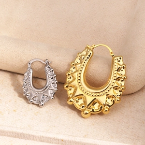 Detalle de pendientes en U dorados y plateados con textura tachonada sobre fondo de tela beige