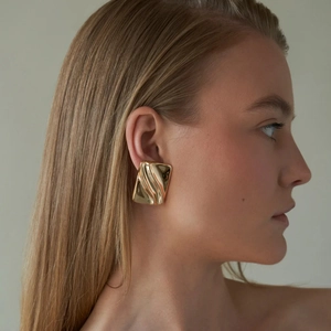 Detail showing the wavy texture and metallic luster of gold rectangular stud earrings