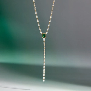 Detalle de un collar en Y dorado con piedra verde de corte esmeralda y cadena de circones